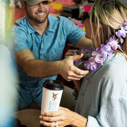 Bad Ass Coffee of Hawaii franchise man places a lei around a woman's neck as she holds her coffee cup